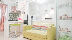 A modern kitchen with a green bar stool, a yellow sofa with patterned cushions, and a glass display case with decorative items. - Elegant 2BR at Bassura City Apartment (Jakarta)