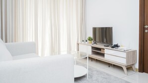 A modern living room with a white sofa, a glass coffee table, a TV on a wooden stand, and a door on the right.