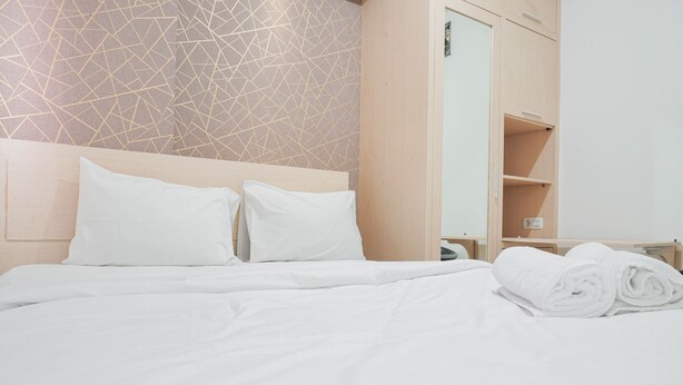 A neatly made bed with white linens and pillows, a wooden headboard, and a wall with a geometric pattern. - Cozy Stay at 2BR Green Pramuka Apartment near Shopping Center (Jakarta)