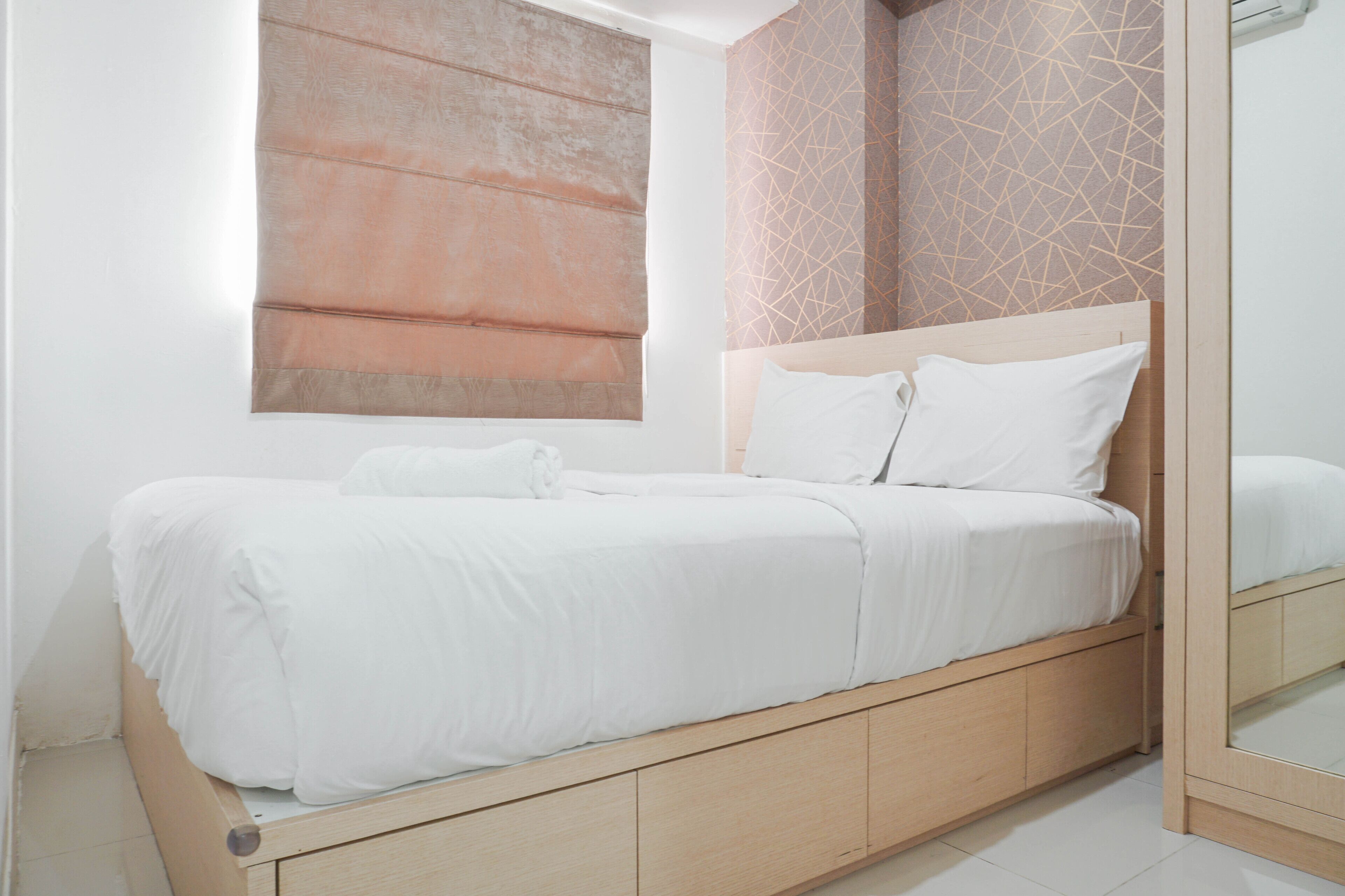 A modern bedroom with a wooden bed frame, white bedding, and a large mirror.
