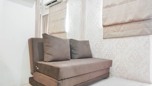 A corner sofa with a cushion, a window with curtains, and a patterned wall. - Cozy Stay at 2BR Green Pramuka Apartment near Shopping Center (Jakarta)