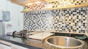 A kitchen with a black countertop, a stainless steel sink, and a tiled backsplash. - Cozy Stay at 2BR Green Pramuka Apartment near Shopping Center (Jakarta)