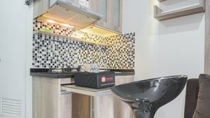 A compact kitchen with a black and white checkered backsplash, a built-in microwave, and a travel bag labeled 'travelio' on the counter. - Cozy Stay at 2BR Green Pramuka Apartment near Shopping Center (Jakarta)