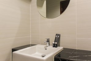A bathroom with a white sink, black countertop, and a round mirror above it. - Scenic Studio at West Vista Apartment Puri (Jakarta)