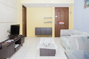 A living room with a sofa, a TV on a stand, a table with a tablecloth, and a door with a sign. - Spacey 2BR Apartment at Great Western Resort (Tangerang)