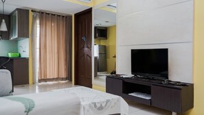 Une chambre d’hôtel équipée d’un lit, d’une télévision, d’un bureau, d’une armoire et d’une salle de bain, visible à travers une porte ouverte.