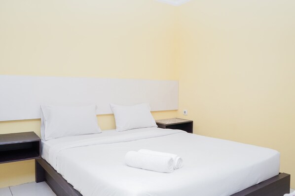 A neatly made bed with white linens and a rolled towel, a bedside table, and a nightstand in a room with yellow walls. - Spacey 2BR Apartment at Great Western Resort (Tangerang)