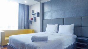A modern hotel room with a large bed, a sofa, and a built-in shelf unit. - Exquisite & Spaciuos 1BR Apartment at Tamansari Papilio (Surabaya)