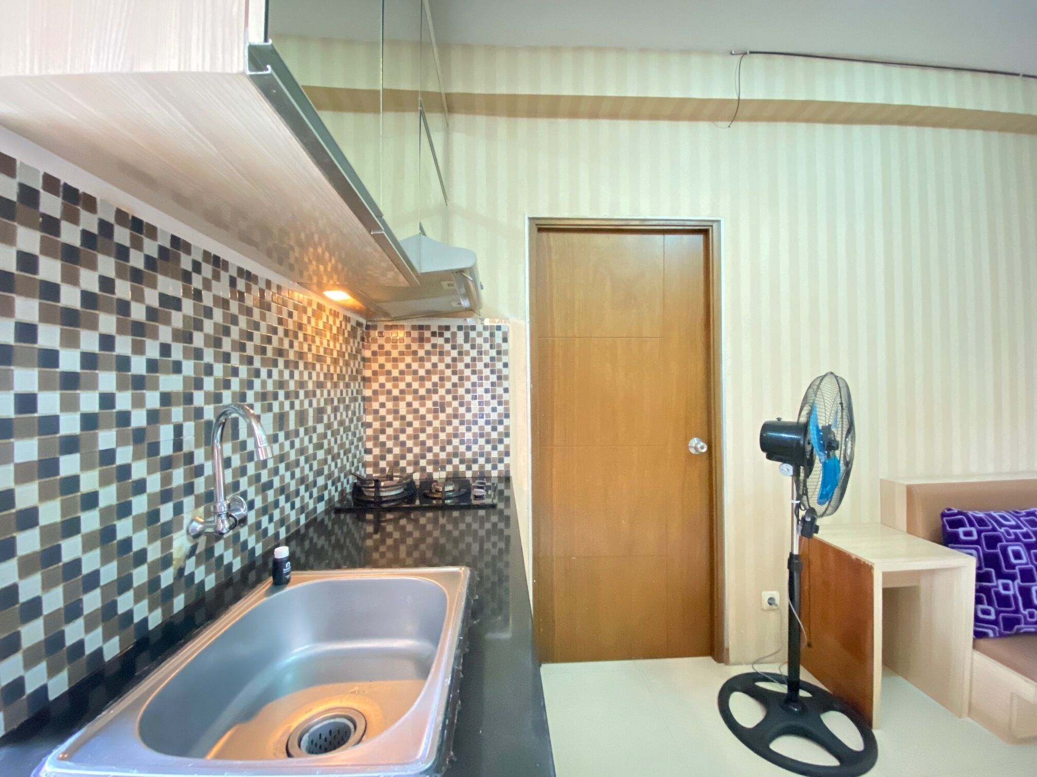 A compact kitchen with a sink, a fan, and a door leading to another room.
