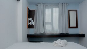 A hotel room with a bed, a window with sheer curtains, a wall-mounted mirror, and a wooden shelf above the bed. - Brand New and Best Choice 2BR at Cinere Resort Apartment (Depok)