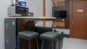 A compact kitchenette with a microwave, kettle, and coffee maker, a small seating area with two stools, a television, and a wooden door with a sign. - Brand New and Best Choice 2BR at Cinere Resort Apartment (Depok)