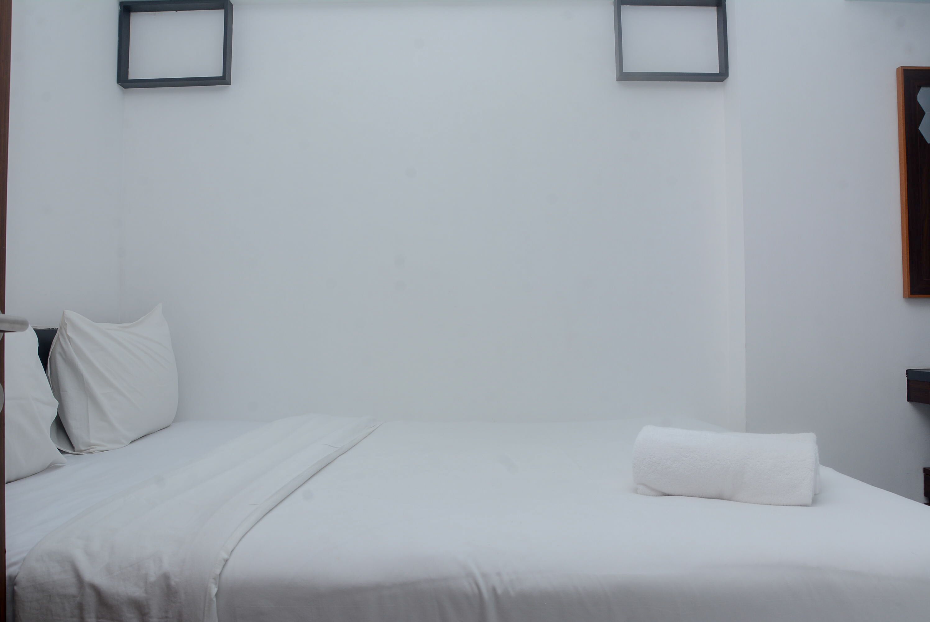 Habitación de hotel minimalista con una cama bien tendida, ropa de cama blanca y una sola almohada.