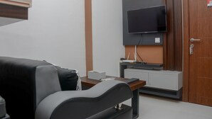 A modern hotel room with a sofa, a flat-screen TV mounted on the wall, a small table with a router, and a wooden door. - Brand New and Best Choice 2BR at Cinere Resort Apartment (Depok)