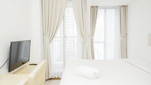 A hotel room with a bed, a TV on a stand, and sheer curtains. - Comfort with Garden View Studio Apartment M-Town Residence (Gading Serpong)