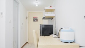 A small, clean room with a wooden table, a black refrigerator, a white kettle, and a wall-mounted shelf. - Comfort with Garden View Studio Apartment M-Town Residence (Gading Serpong)