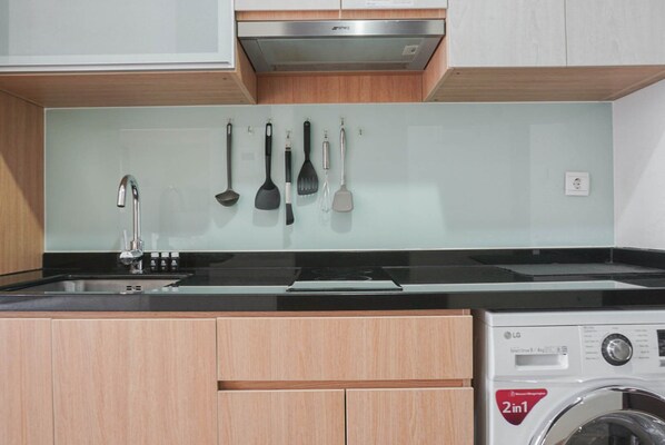 A compact kitchen with a washing machine, wooden cabinets, and a stainless steel range hood.
