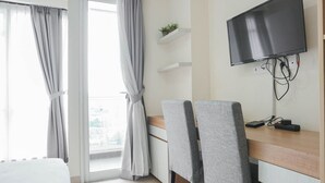 Ein modernes Zimmer mit Schreibtisch, zwei grauen Stühlen, einem Wand-Fernseher und einem Balkon mit grauen Vorhängen.