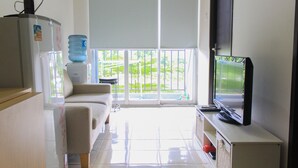 A living room with a sofa, a television, a water dispenser, and a sliding glass door to a balcony. - Comfy and Best View 2BR at Serpong Greenview Apartment (South Tangerang)