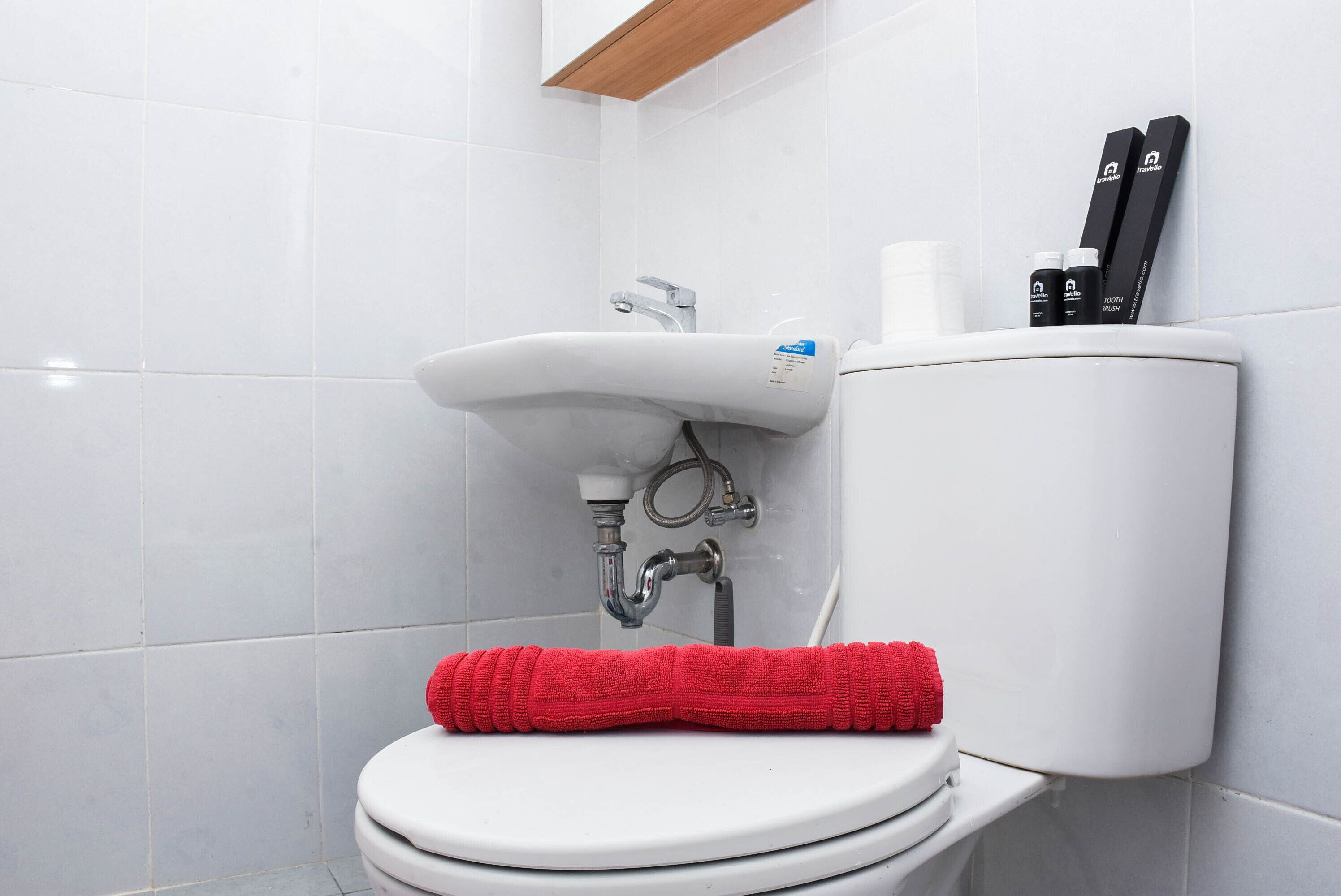 A white toilet with a red towel, a white sink, and two black bottles on the wall.