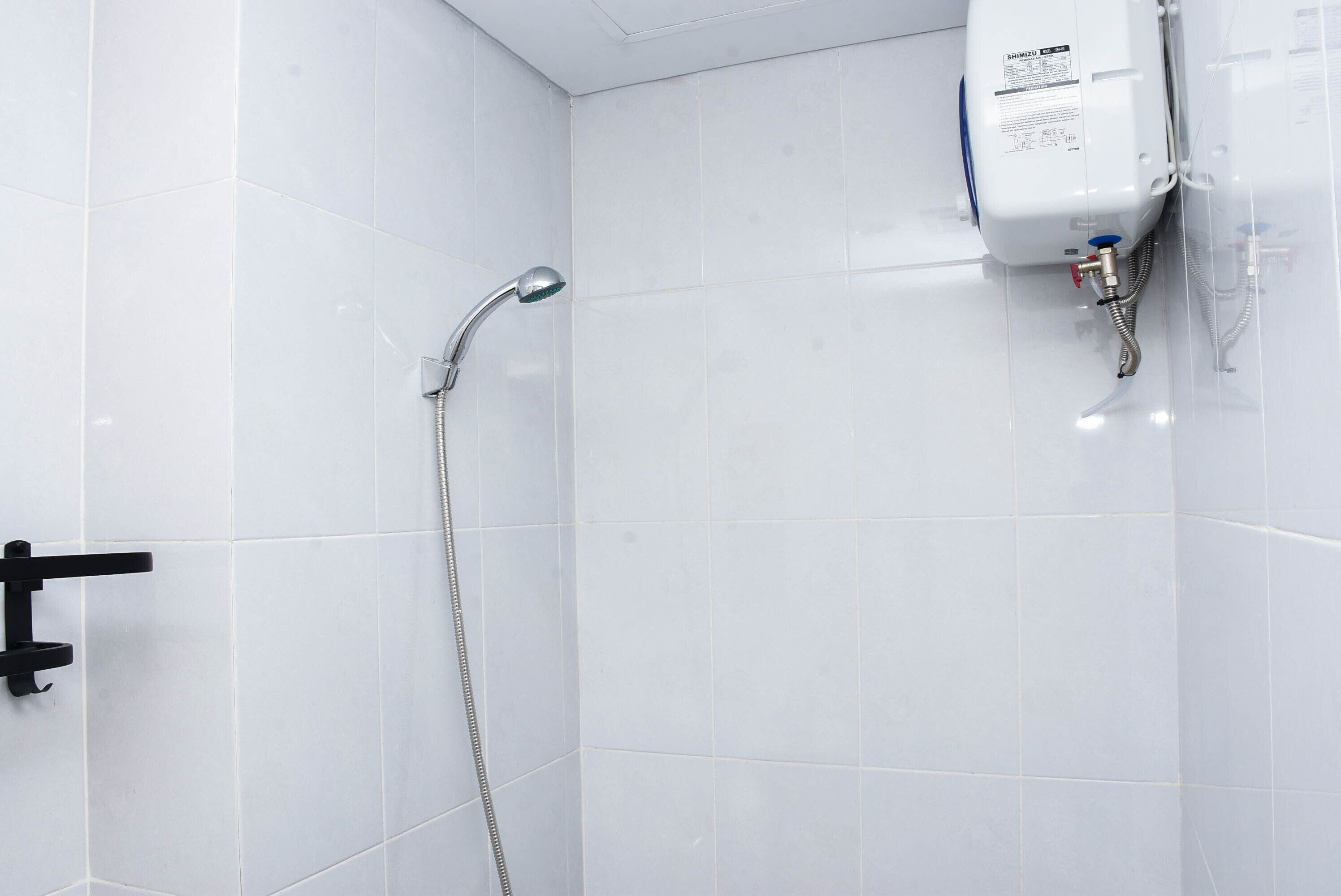 A shower area with white tiled walls and a handheld showerhead.