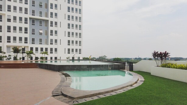 Un edificio moderno con piscina en la azotea, rodeado de vegetación y un cielo despejado.