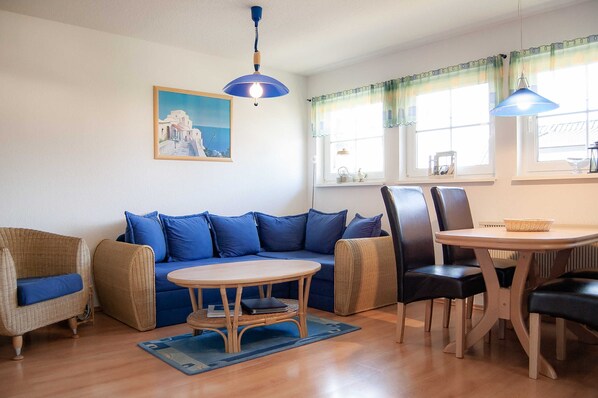 A cozy living room with a blue sofa, wicker armchairs, a wooden coffee table, and a dining table with chairs.