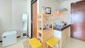 Cozinha compacta com geladeira, prateleira de madeira com panelas, pia e dois banquinhos amarelos.