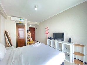 Habitación de hotel con cama, televisión, estante y perchero.