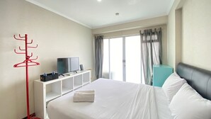 Quarto de hotel com uma cama, uma televisão sobre um suporte branco, um porta-roupas vermelho e uma janela com cortinas.