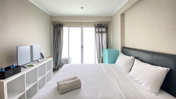 Quarto de hotel com cama, televisão em móvel, armário azul e janela com cortinas.