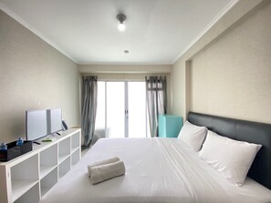 Una habitación de hotel con una cama, un televisor sobre un soporte, un armario azul y una ventana con cortinas.