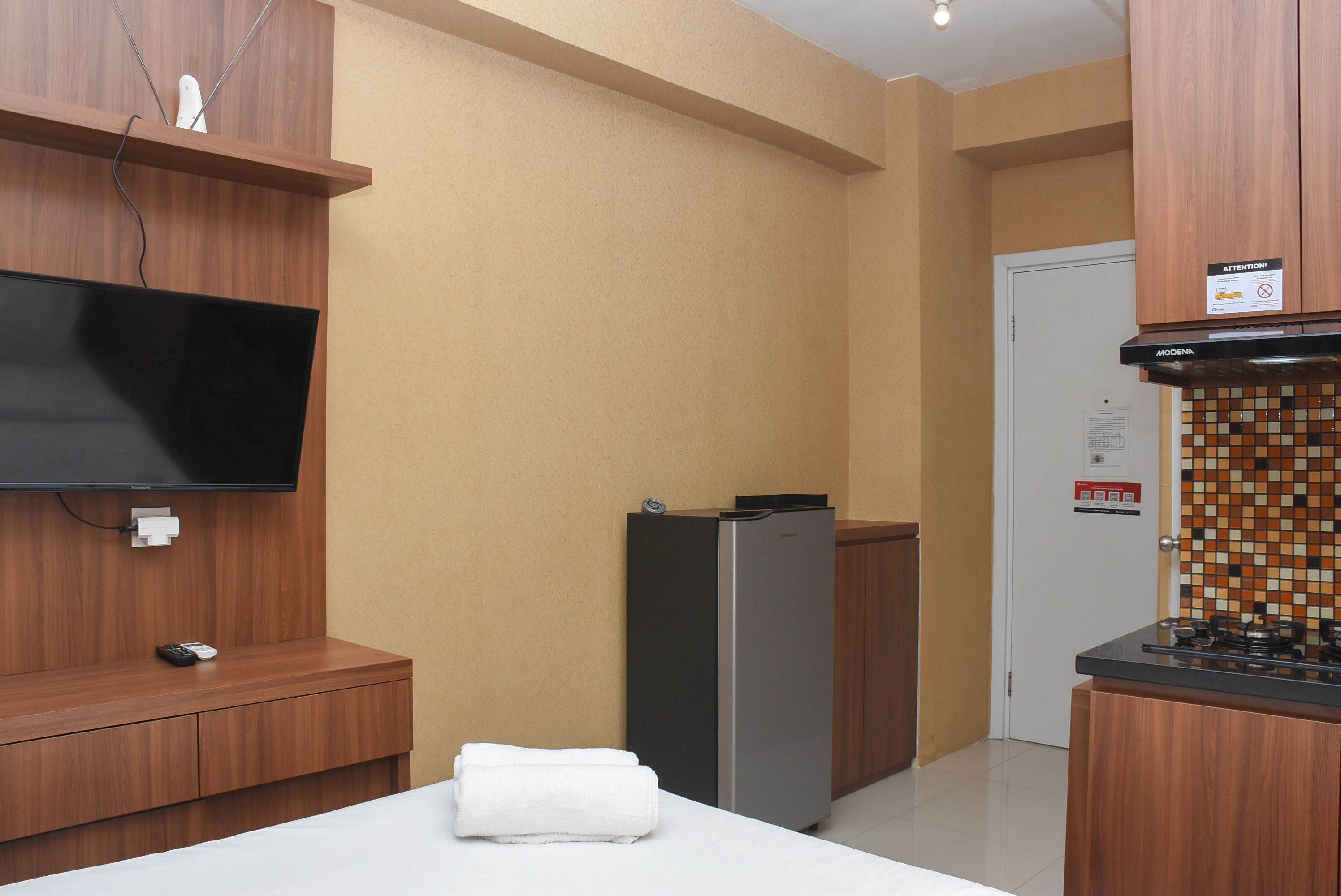 Une chambre d’hôtel équipée d’un téléviseur à écran plat fixé au mur, d’un petit réfrigérateur, d’une armoire en bois et d’un revêtement mural en carreaux près de la porte.