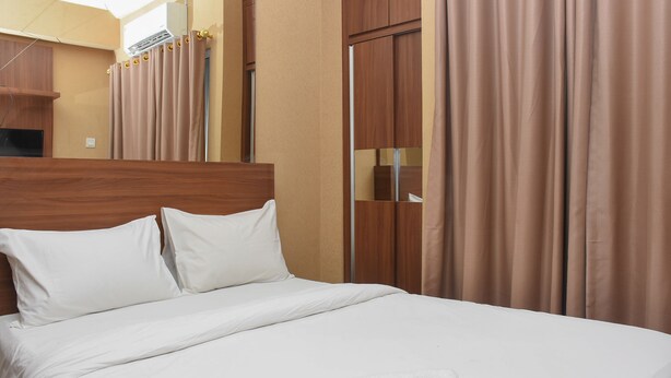 Uma cama bem arrumada com lençóis brancos, cabeceira de madeira e dois travesseiros brancos.