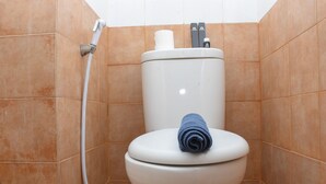Uma casa de banho com azulejos laranja, sanita com uma toalha no assento, rolo de papel higiénico e chuveiro bidé.