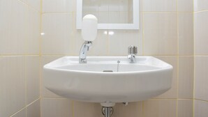 Un lavabo bianco con due rubinetti, uno specchio sopra e pareti rivestite di piastrelle gialle.