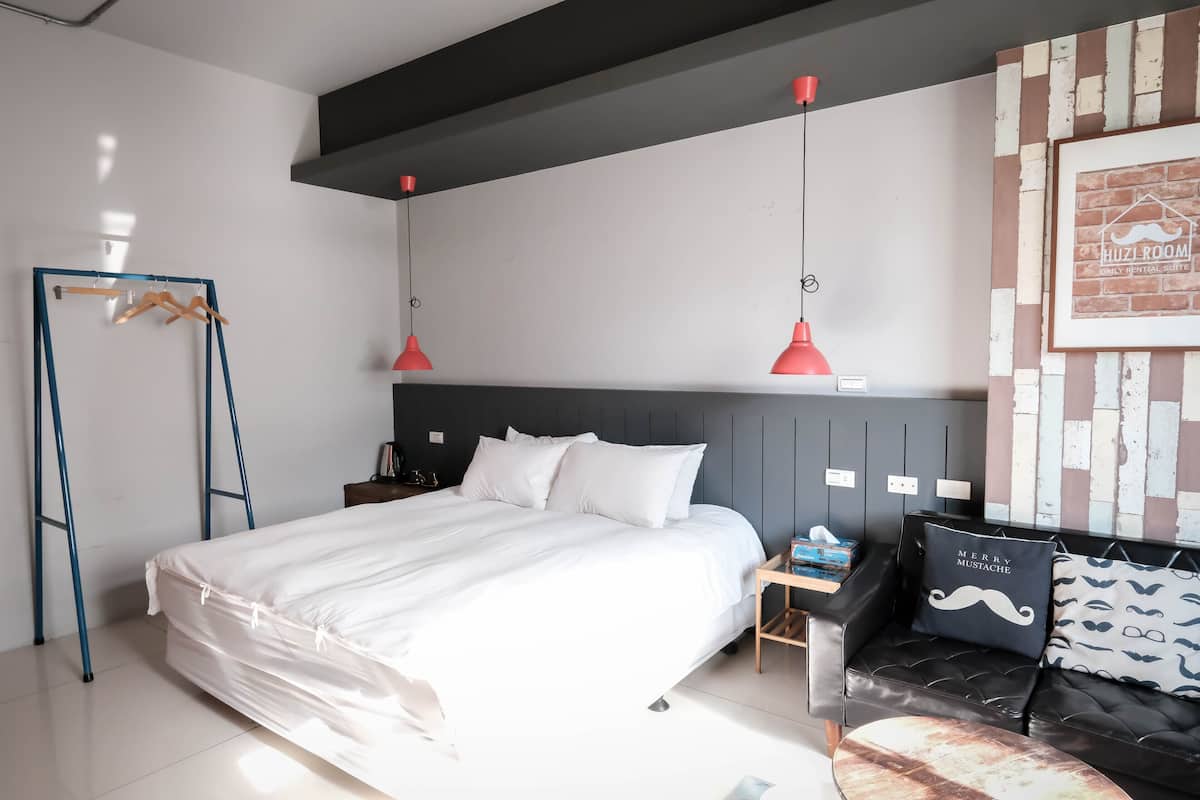 A modern bedroom with a large bed, a black leather sofa, and a red pendant light.