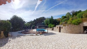 Une cour avec un sol en pierre, une piscine et un espace salon abrité.