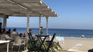Un café situé en bord de mer, avec une terrasse, une vue sur l’océan et une pergola en bois.