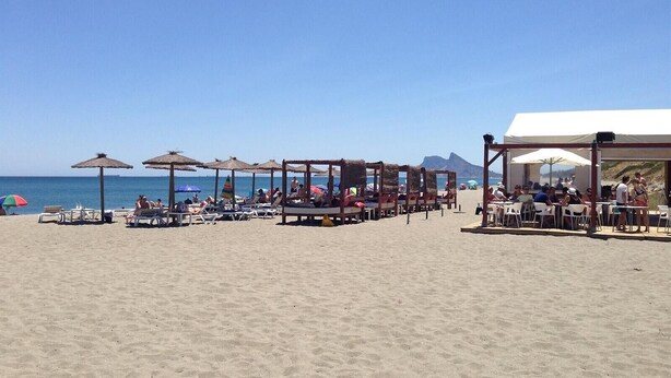 Une plage avec des chaises longues, des parasols et un espace abrité équipé de tables et de chaises.