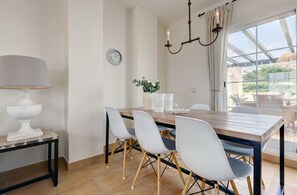 A dining area with a wooden table, white chairs, a white lamp, and a clock on the wall. - Penthouse Apartment in Alcaidesa with Mountain View, Wi-Fi, Pool, Garden & Terrace (Alcaidesa)