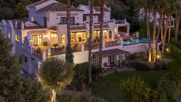 Une grande maison à plusieurs étages, dotée d’une piscine, entourée de palmiers et d’un jardin bien entretenu.
