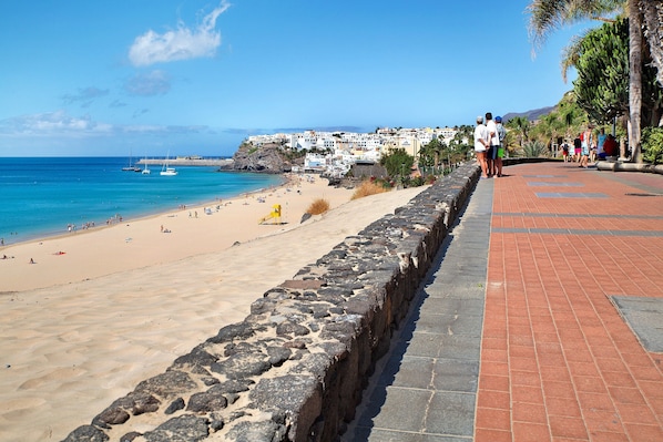 A beach with a stone wall, a paved walkway, and buildings in the background.