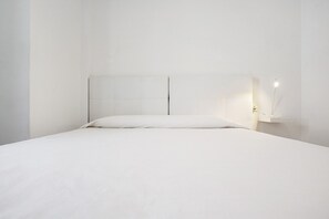 A minimalist bedroom with a large bed, a simple headboard, and a bedside table with a lamp.