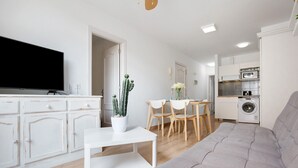 A modern living room with a grey sofa, a flat-screen TV, a dining area with a table and chairs, and a kitchen with appliances. - Vacation Apartment "Playa Morro Jable 1c" near the Beach with Wi-Fi (Morro Jable)