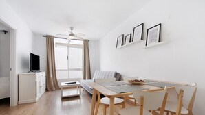 Een moderne woonkamer met een bank, een eettafel met stoelen, een televisie op een kast en een plafondventilator.