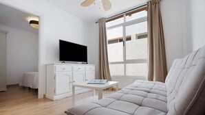 Een moderne woonkamer met een bank, een televisie op een kast, een bijzettafeltje en een raam met gordijnen.
