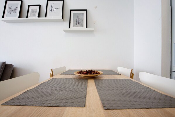 A dining area with a wooden table, two gray placemats, a bowl of food, and framed artwork on the wall.