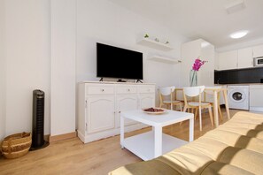 Un salon moderne avec un téléviseur à écran plat, un meuble blanc, une petite table avec un saladier, un canapé, un lave-linge et un ventilateur de plafond.