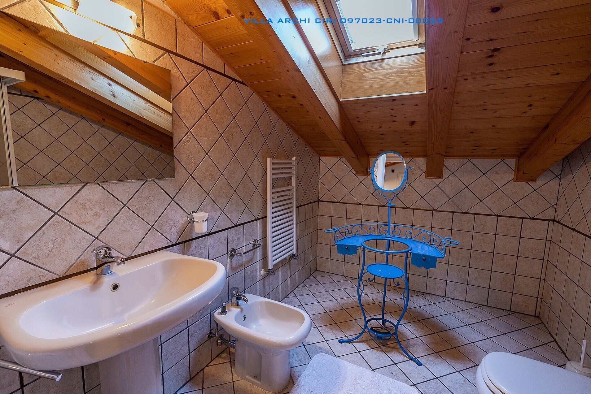 A bathroom with a skylight, a white sink, a bidet, a blue pedestal sink, and a toilet.