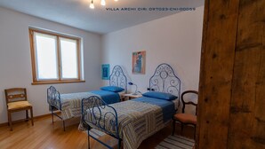 Une pièce avec deux lits à ossature métallique, une chaise en bois, une petite table et une fenêtre.